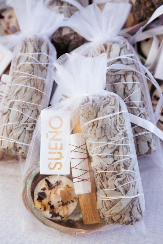 Sueño Smudge Bundle in a white organza gift bag with white sage, palo santo wrapped in selenite, abalone shell and tea light candle